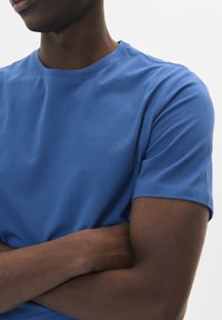 Camiseta de algodón azul con cuello redondo y mangas cortas, que presenta una textura suave y sin patrones o acentos visibles.
