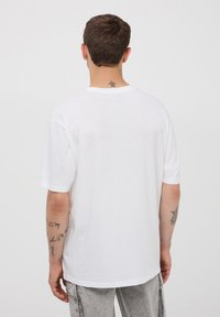 Biała bawełniana koszulka z krótkim rękawem, luźny fason i okrągły dekolt. Posiada gładką fakturę oraz minimalistyczny design.