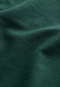 Tissu doux vert foncé avec une texture fine de tricot visible et des plis subtils créant de douces ombres.