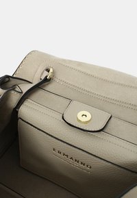Interno di una borsa in pelle beige chiaro con un rivestimento testurizzato, chiusura a scatto dorata e logo del brand impresso. Presenta un bordo nero a contrasto.