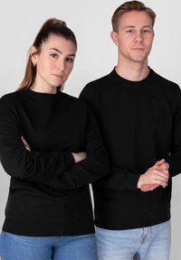 Sweatshirts noirs à col rond en tissu doux, avec des manches longues et des poignets côtelés, portés par deux individus sur un fond uni.