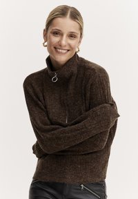 Brauner Strickpullover mit hohem Kragen und Reißverschlussdetail. Weiche Textur und lockere Passform, mit weiten Ärmeln und Rippmuster.