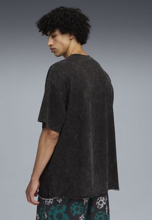 Schwarz übergroßes T-Shirt mit einem abgenutzten Look, kurzen Ärmeln, Rundhalsausschnitt und einer strukturierten Oberfläche. Getragen mit bedruckten Shorts mit floralen Mustern.