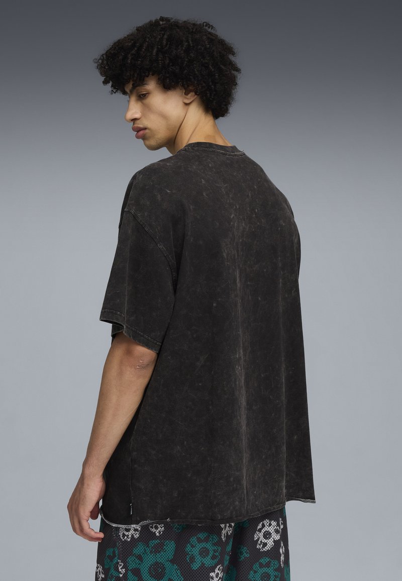 Černé oversized tričko s distressed vzhledem, krátké rukávy, kulatý výstřih a texturovaný povrch. Nosené s tištěnými šortkami s květinovými vzory.