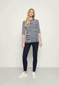 Top às riscas, de mangas três quartos, em azul marinho e branco, combinado com leggings escuras e ténis brancos. Tecido suave com design ajustado.