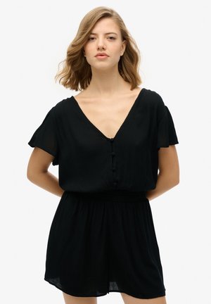 Robe-pantalon noire avec un décolleté en V, des manches courtes et évasées, des boutons décoratifs et une taille élastique pour un ajustement décontracté. Tissu doux et léger.