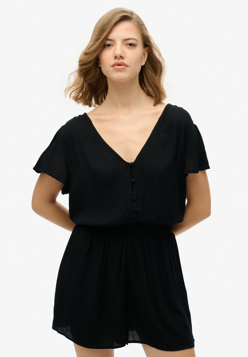 Mono negro con escote en V, mangas cortas tipo volante, botones decorativos y una cinturilla elástica para un ajuste relajado. Tejido suave y ligero.
