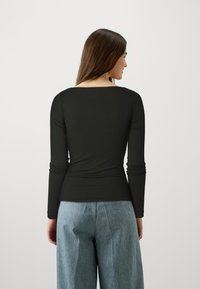 Zwarte langmouwen top met een vierkante halslijn en een aansluitende silhouet, gecombineerd met lichtblauwe wijde broek. Gladde textuur, minimalistisch ontwerp.
