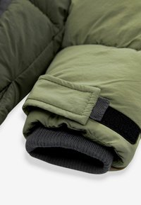 Funda acolchada de color verde oliva con puño elástico negro y correa de Velcro, que presenta una textura lisa y mate y un patrón de acolchado distintivo.