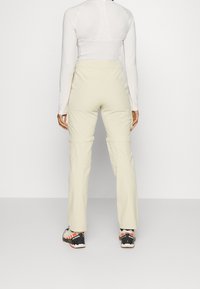 Beige utomhusbyxor med en avslappnad passform, tillverkade av lättviktig tyg; har dragkedjefickor och justerbara benslut för mångsidighet.