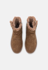 Botas de tobillo de ante marrón con un cuello de piel sintética, interior forrado y costuras decorativas a lo largo de la suela. Diseño plano y casual para el clima frío.