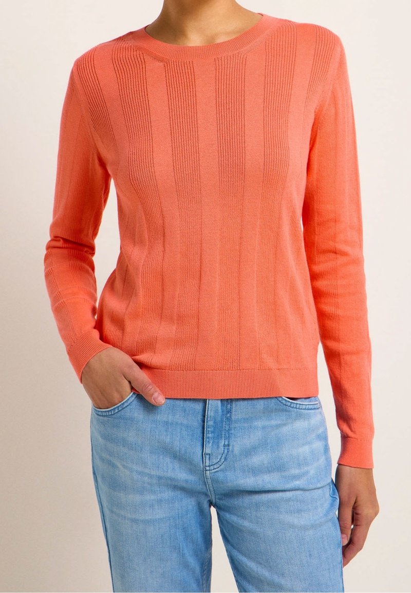 Coral-knit sweater with ribbed texture, round neckline, and long sleeves, paired with light blue denim jeans.