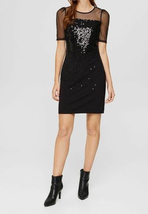 Czarna sukienka z cekinowym gorsetem i przezroczystymi krótkimi rękawami, dopasowana sylwetka, o długości powyżej kolana, w połączeniu z czarnymi botkami za kostkę.