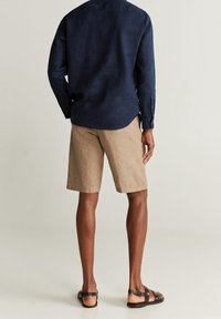 Camicia a maniche lunghe in lino navy, pantaloni corti in lino beige e sandali in pelle marrone. Cuciture visibili e vestibilità rilassata sia nella parte superiore che in quella inferiore.