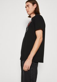 Zwarte t-shirt met korte mouwen, voorzien van een grafisch ontwerp in rood en wit op de voorkant. Gemaakt van zachte stof met een relaxte pasvorm.