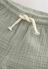 Lichtgroene katoenen korte broek met een gestructureerde afwerking. Voorzien van een elastische tailleband en een crèmekleurige trekkoord met een knoop.