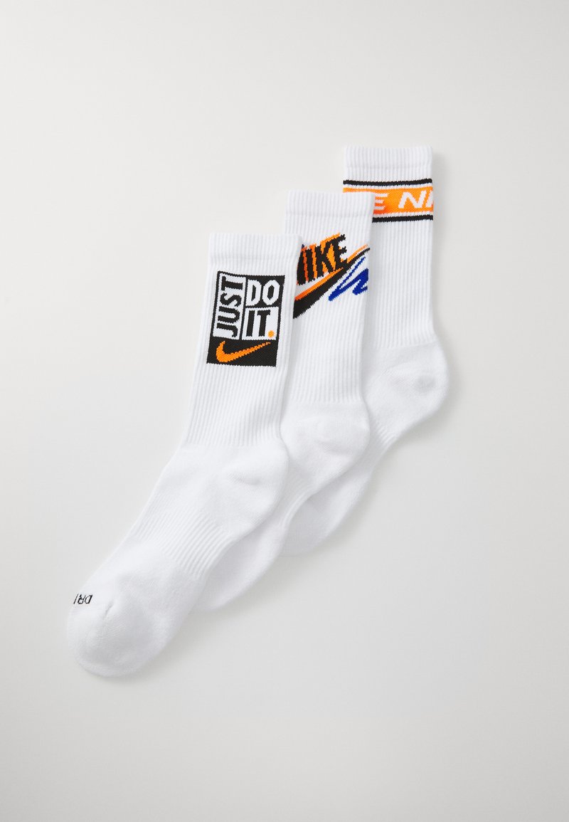 Tři páry bílých ponožek s kontrastními černými a oranžovými logy: "JUST DO IT," "NIKE," a proužkované akcenty. Rýhovaná textura.