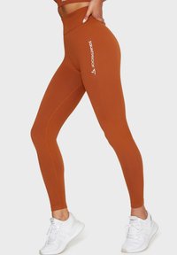 Wysokie legginsy sportowe w kolorze rdzy, z prążkowaną teksturą i białym napisem "SQUATPROOF" wzdłuż boku.