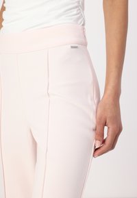 Helle rosa maßgeschneiderte Hosen mit einer glatten Textur, ausgestattet mit einem breiten Bund und einem dezenten Markenetikett auf der Vorderseite. Das schlanke Design betont die Form.