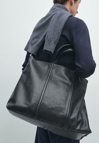 Zwarte leren tote bag met een slank ontwerp, gladde textuur en twee stevige zijhandvatten. Kenmerkt zich door naaddetails en een ruime binnenkant.