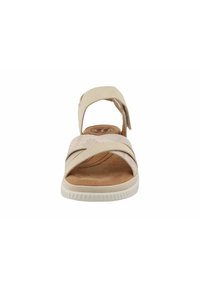 Beige sandal featuring a cross-strap design, adjustable ankle strap, textured footbed, and a rubber sole with a ridged pattern.