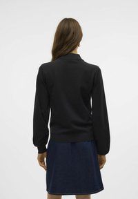 Pull noir avec de longues manches bouffantes et un col ; associé à une jupe en denim foncé. Le tissu semble lisse et ajusté à la taille.