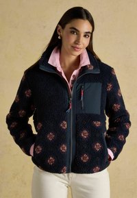 Fleecejacket in navy met een gestructureerd patroon van lichtbruine en bordeauxrode stippen. Voorzien van een ritssluiting aan de voorkant en een borstzak met accenten van ritsen.