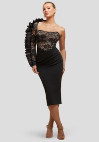 Sort kjole med en blondeoverdel, ét ærme prydet med plisserede detaljer og en tætsiddende silhuet, der når til knæet.