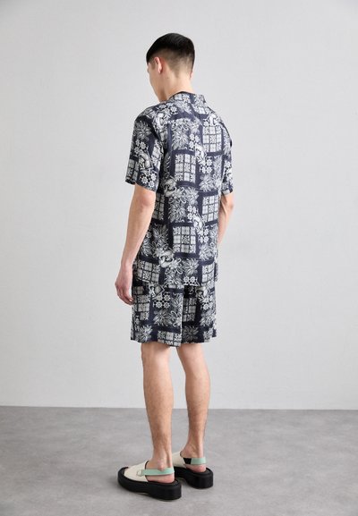 Short-sleeve dark floral print shirt with matching shorts, made of lightweight fabric. Worn with chunky sandals featuring a two-tone design.