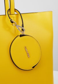 Żółta torebka tote z teksturowanej skóry z pasującą okrągłą kieszonką na monety przymocowaną złotym zapięciem, z logo Calvin Klein na kieszonce.