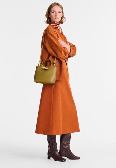 Orange suede shirt and matching long skirt, paired with knee-high burgundy boots and a small olive handbag with a circular handle.