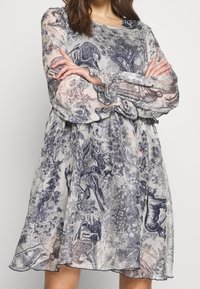 Průhledné šaty s vzorem a dlouhými rukávy, zdobené modro-krémovým zvířecím designem. A-liniový tvar s nařasenými manžetami a lemem.