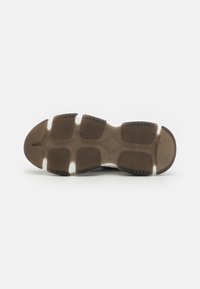 Shoe sole with textured brown rubber, featuring a wavy pattern and white accent pieces, designed for traction and durability.