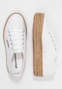 White canvas sneakers with woven jute platform sole, featuring lace-up design, silver eyelets, and branded insole.