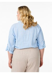 Camicia a righe azzurro chiaro con maniche a tre quarti, dotata di risvolti. Abbinata a pantaloni beige con vita elastica. Tessuto strutturato.