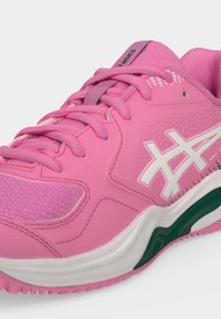 Ροζ αθλητικό παπούτσι ASICS με λευκό λογότυπο, υφασμάτινη επιφάνεια με υφή και σόλα με πράσινες λεπτομέρειες, εμφανιζόμενο από κοντινή γωνιακή άποψη.