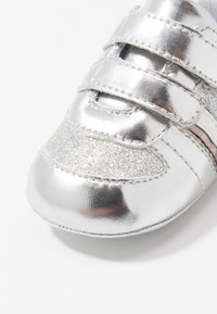 Silberne metallische Sneaker mit strukturierten Glitzerakzenten, runder Schuhspitze und drei Klettverschlüssen im Obermaterial für einen sicheren Sitz.