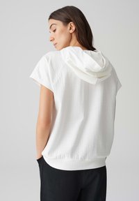 Felpa bianca a maniche corte con design testurizzato e cappuccio con coulisse. Presenta una vestibilità comoda e un orlo a coste.