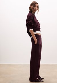 Felpa bordeaux e pantaloni a gamba larga coordinati, realizzati in un tessuto morbido, con una camicia in cotone bianco a strati sotto e tasche laterali.