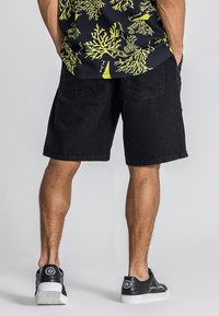 Shorts de mezclilla negra con un corte relajado, dos bolsillos traseros y un dobladillo justo por encima de la rodilla, combinados con zapatillas negras.