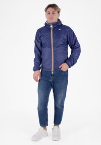 Softshell navy con zip anteriore e cappuccio, con zip accentuata in oro. Abbinato a jeans in denim chiaro e sneakers bianche.