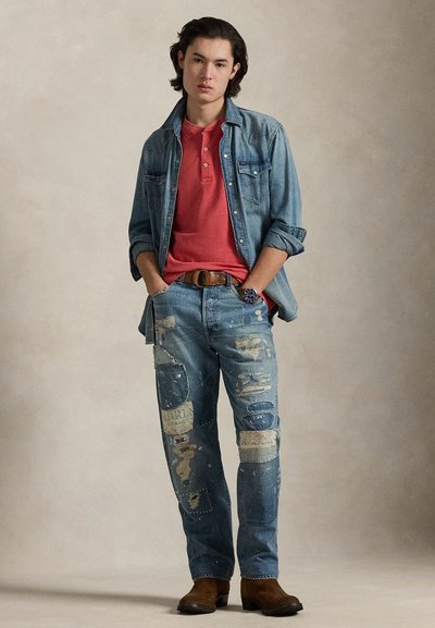 Τζιν πουκάμισο πάνω από κόκκινο πόλο, σε συνδυασμό με σκισμένο τζιν παντελόνι με πολλαπλά μπαλώματα. Καφέ μπότες ολοκληρώνουν το σύνολο.