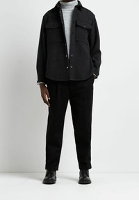 Mörkgrå överdimensionerad skjorta med två bröstfickor och tryckknappar, överlagd på en ljusgrå polotröja. Svarta byxor och stövlar fulländar looken.