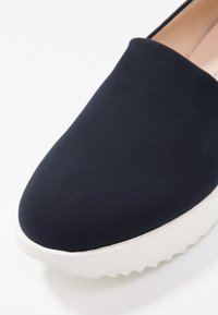 Marine instapschoen met een soepele stoffen bovenkant en een dikke, witte, gestructureerde zool. Rond neuzen, minimalistisch ontwerp, geen zichtbare accenten.