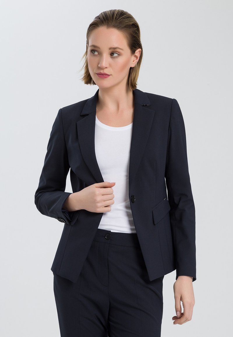 Navy blazer with a tailored fit, two front pockets, single button closure, and notched lapels, worn over a white top.