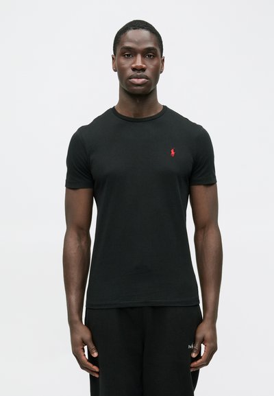 Fekete pamut póló környakú és rövid ujjú, a mellkason apró, piros hímzett logóval. Simaságú anyag.