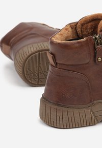 Bottes chelsea en cuir marron avec une finition texturée, doublure en fourrure et semelle en caoutchouc avec des rainures pour une bonne traction. Détail de fermeture éclair sur le côté.