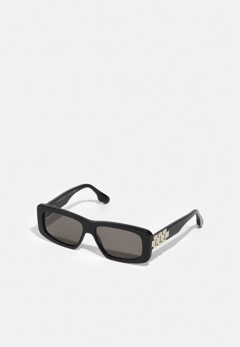 Gafas de sol rectangulares negras con lentes grises. Presentan montura gruesa y acentos metálicos en las patillas, diseñadas para un aspecto audaz.