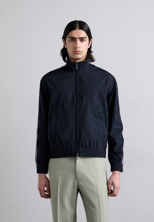 Marineblå zip-up jakke med høj krave, elastiske manchetter og forlommer. Har kontrasterende striber langs ærmerne.