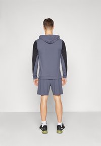 Grå atletisk hoodie med sorte ærmer, kombineret med matchende shorts. Har en hætte og en glat tekstur, velegnet til aktivt tøj.